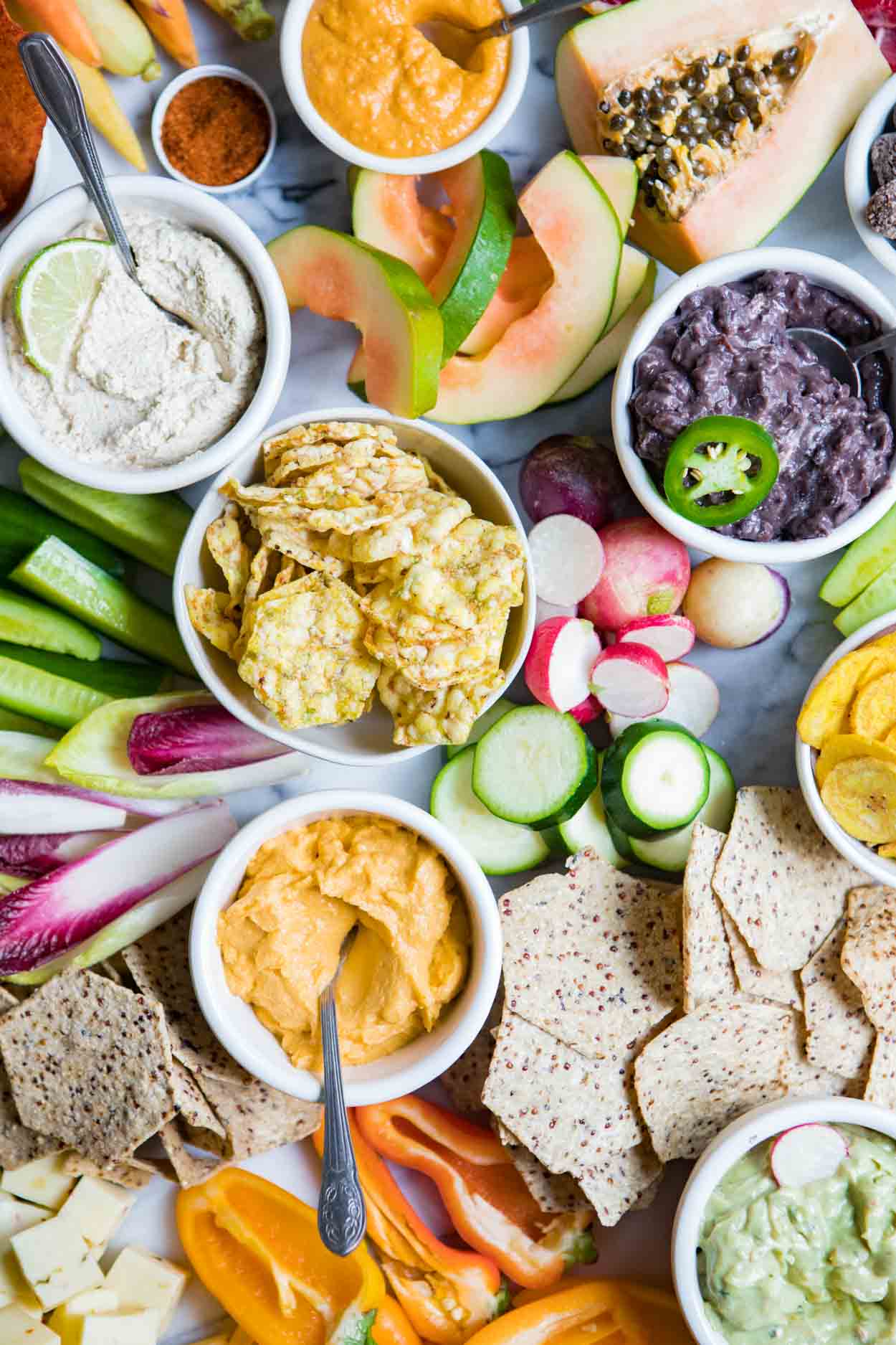 close up photo of fancy fruits and vegetables and crackers on a marble board for a crudite platter