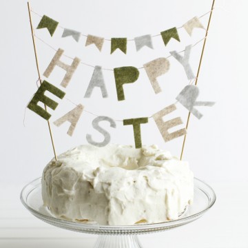 White frosted cake on a glass pedestal stand with a felt happy Easter banner