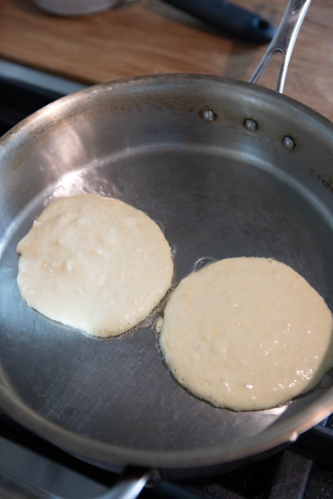 pancakes being cooked in a stainless steel pan 