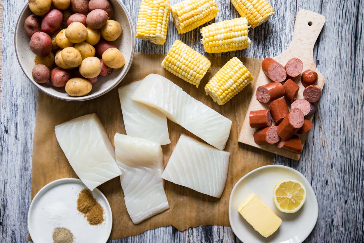 ingredients for halibut sheet pan dinner with fish, corn, sausage and potatoes