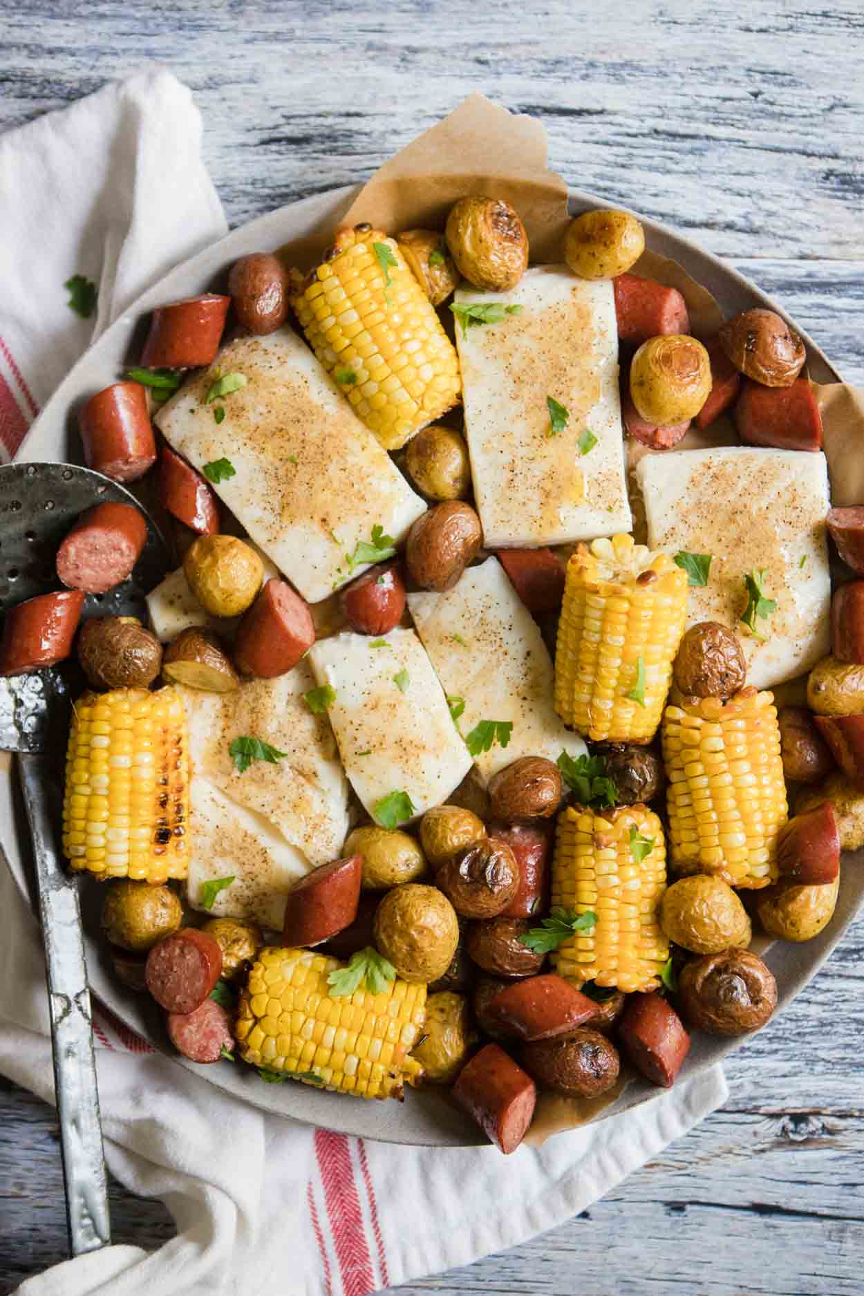 close up of a round platter filled with corn, sausage, halibut and potatoes 