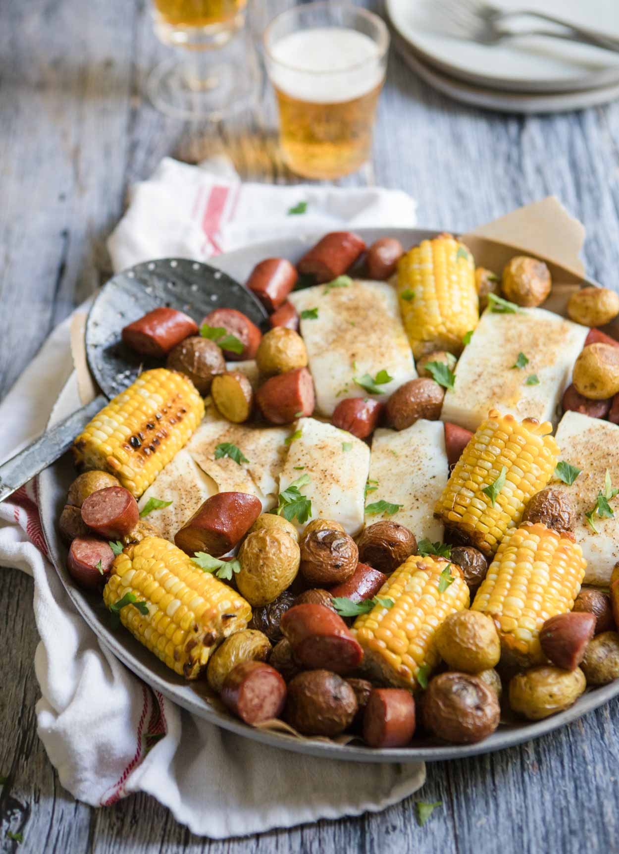 sausage sheet pan dinner with pieces of halibut, corn and potatoes set against a gray backdrop