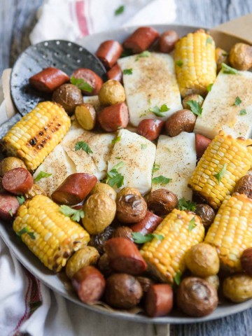 halibut, sausage, corn and potatoes on a round platter with seasoning on top