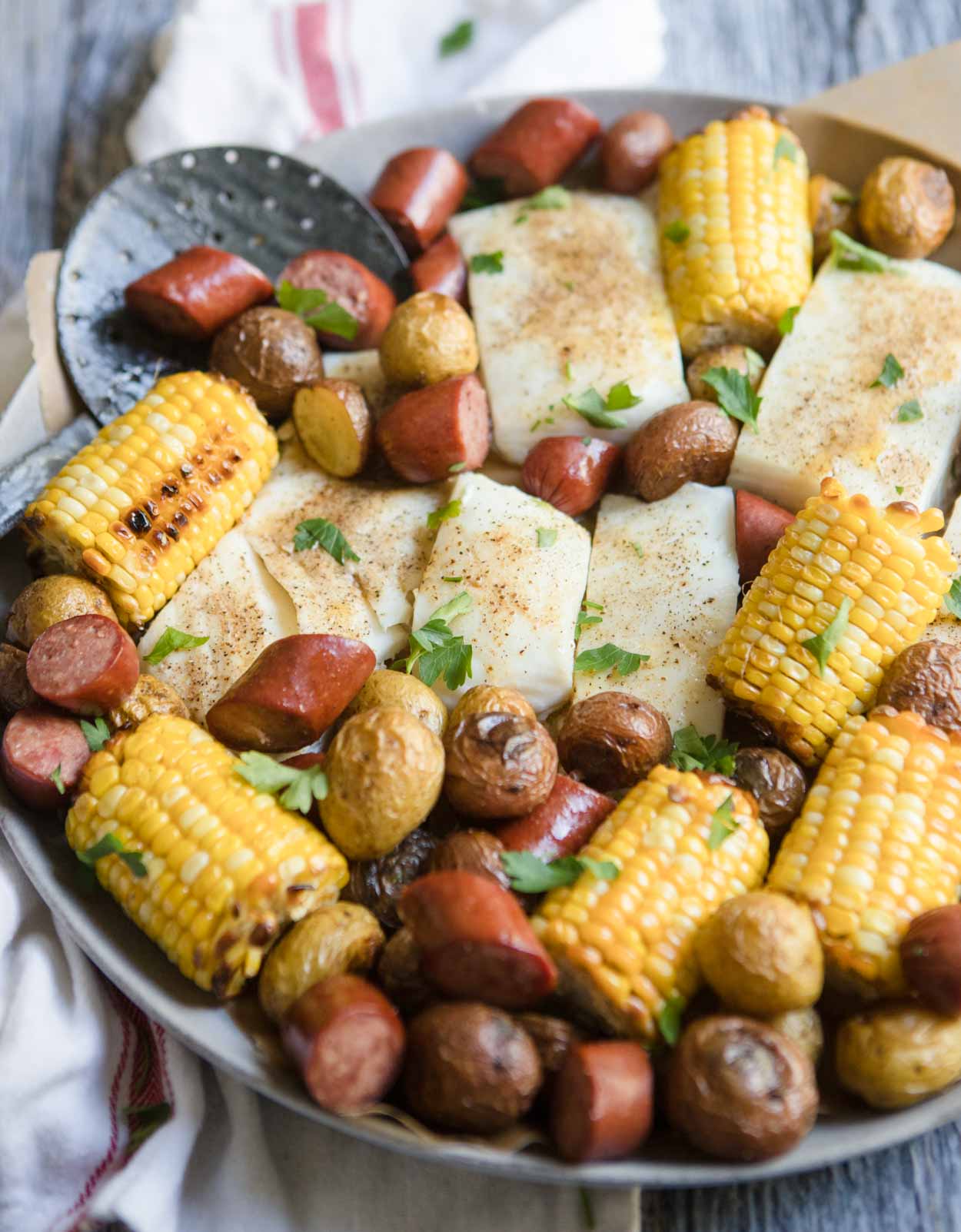 sausage sheet pan with halibut, corn and potatoes on a round platter with seasoning on top