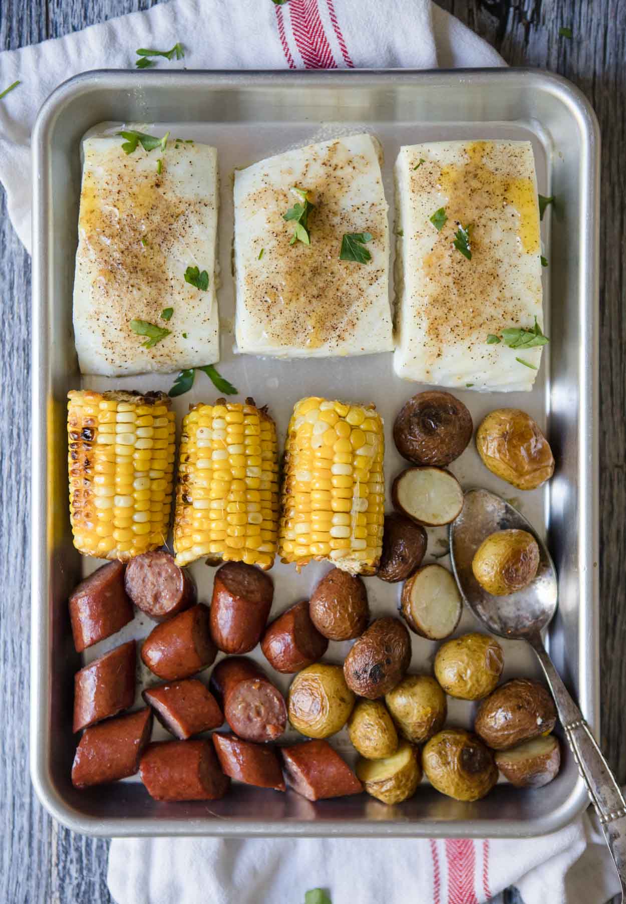 halibut, corn, sausage, and potatoes on a silver baking tray 