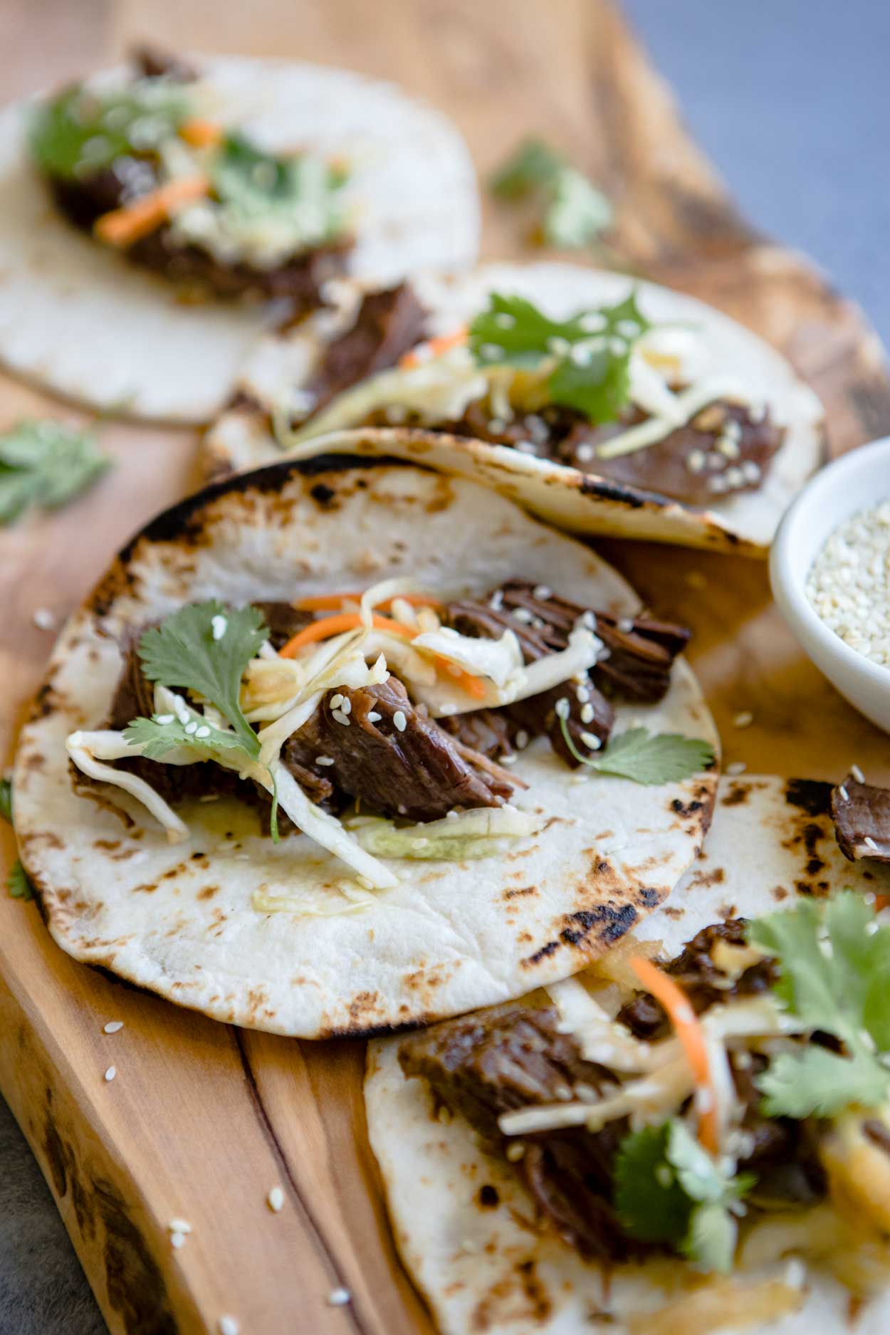 close up shot of beef tacos with shredded cabbage on top, on a wooden board