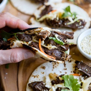 close up picture of a man holding a korean beef taco over a wooden board