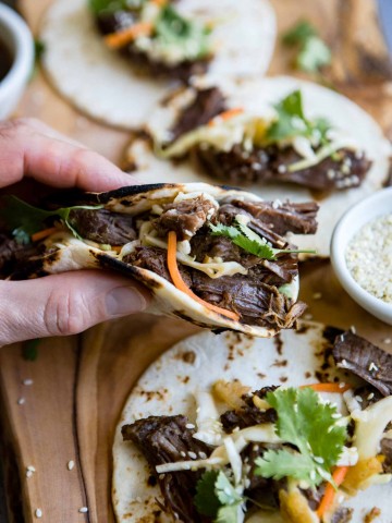 close up picture of a man holding a korean beef taco over a wooden board