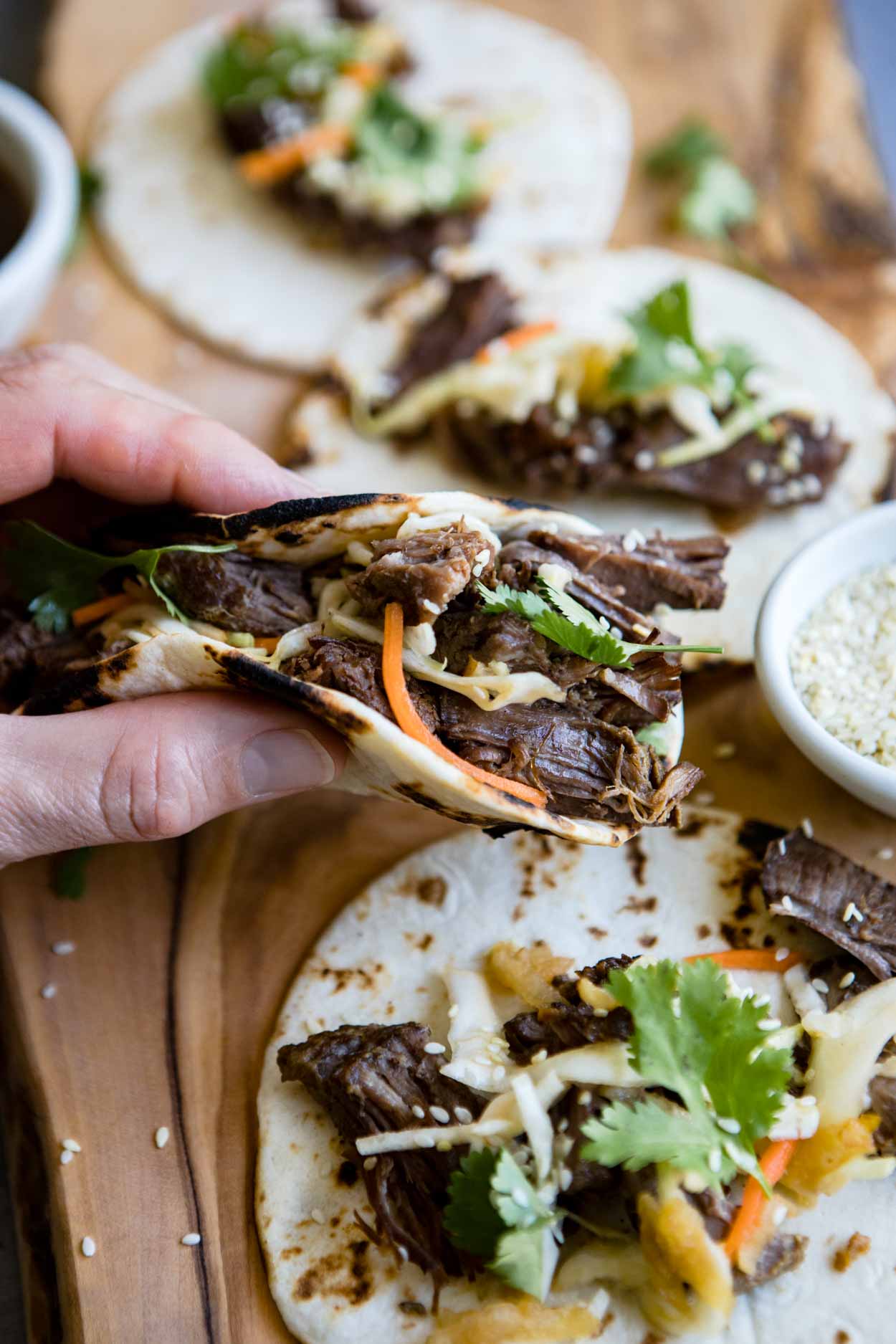 close up picture of a man holding a korean beef taco over a wooden board