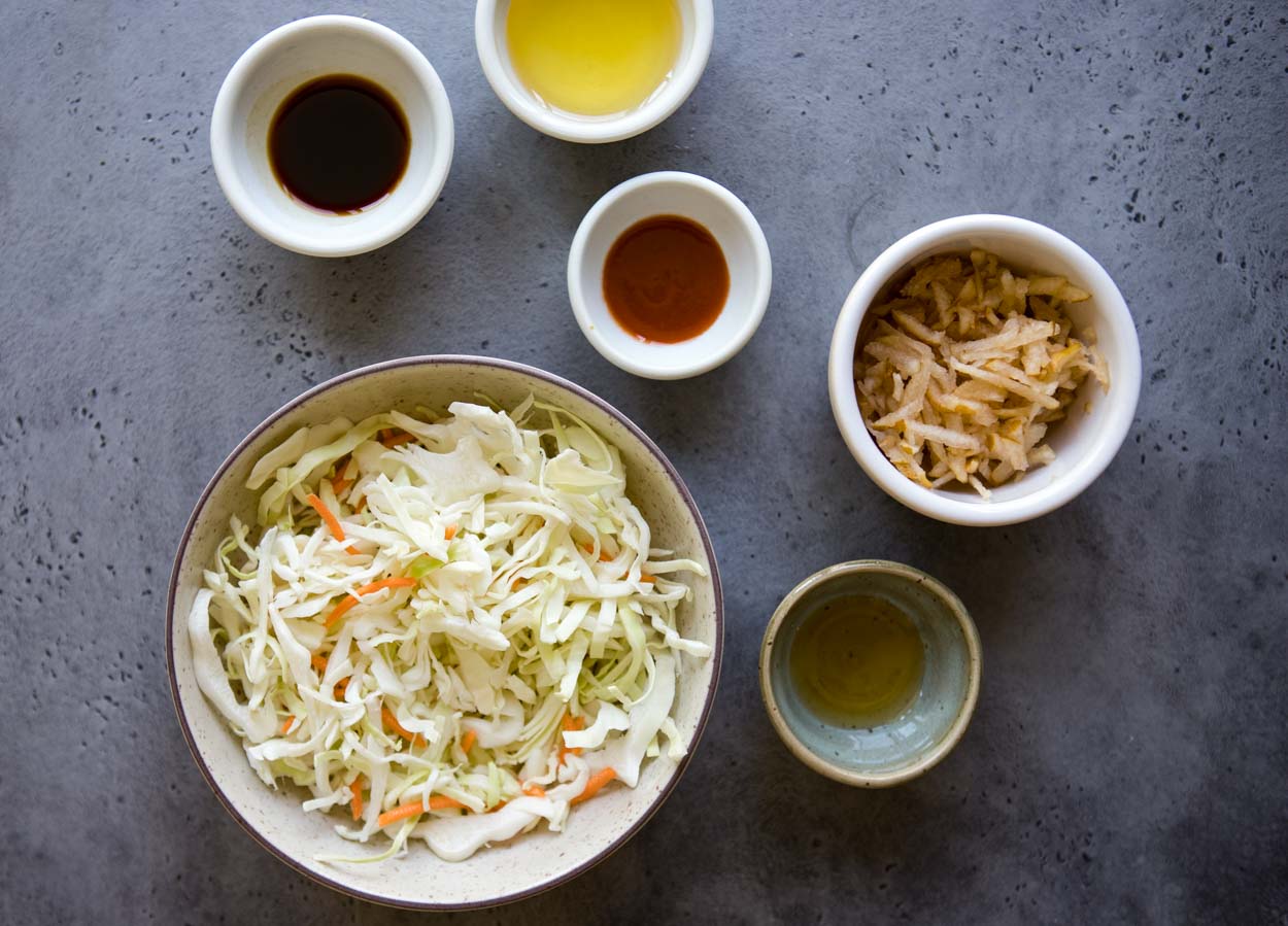 Coleslaw ingredients in round bowls on a gray background