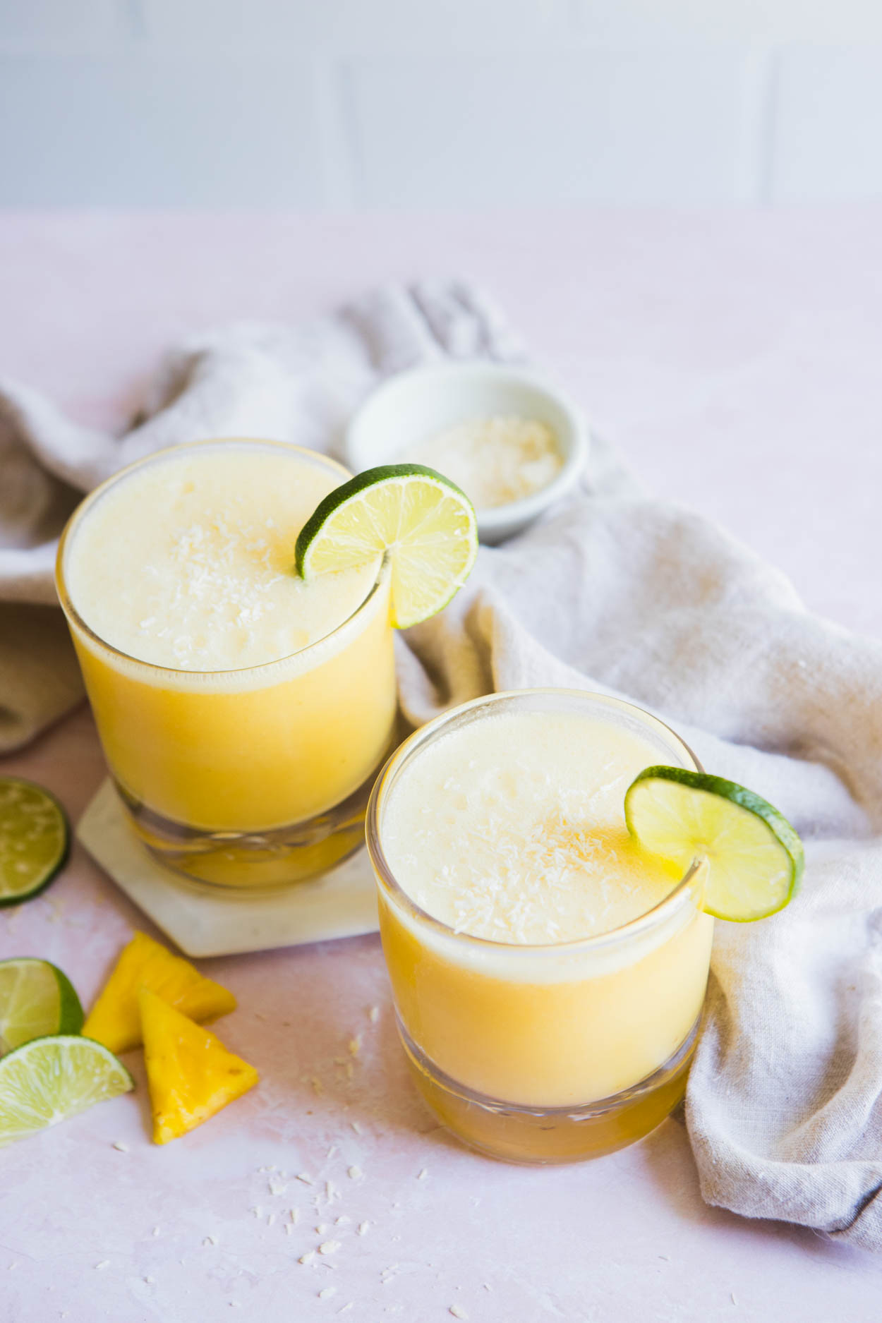 2 clear glasses filled with pineapple coconut margarita and a lime wedge garnish