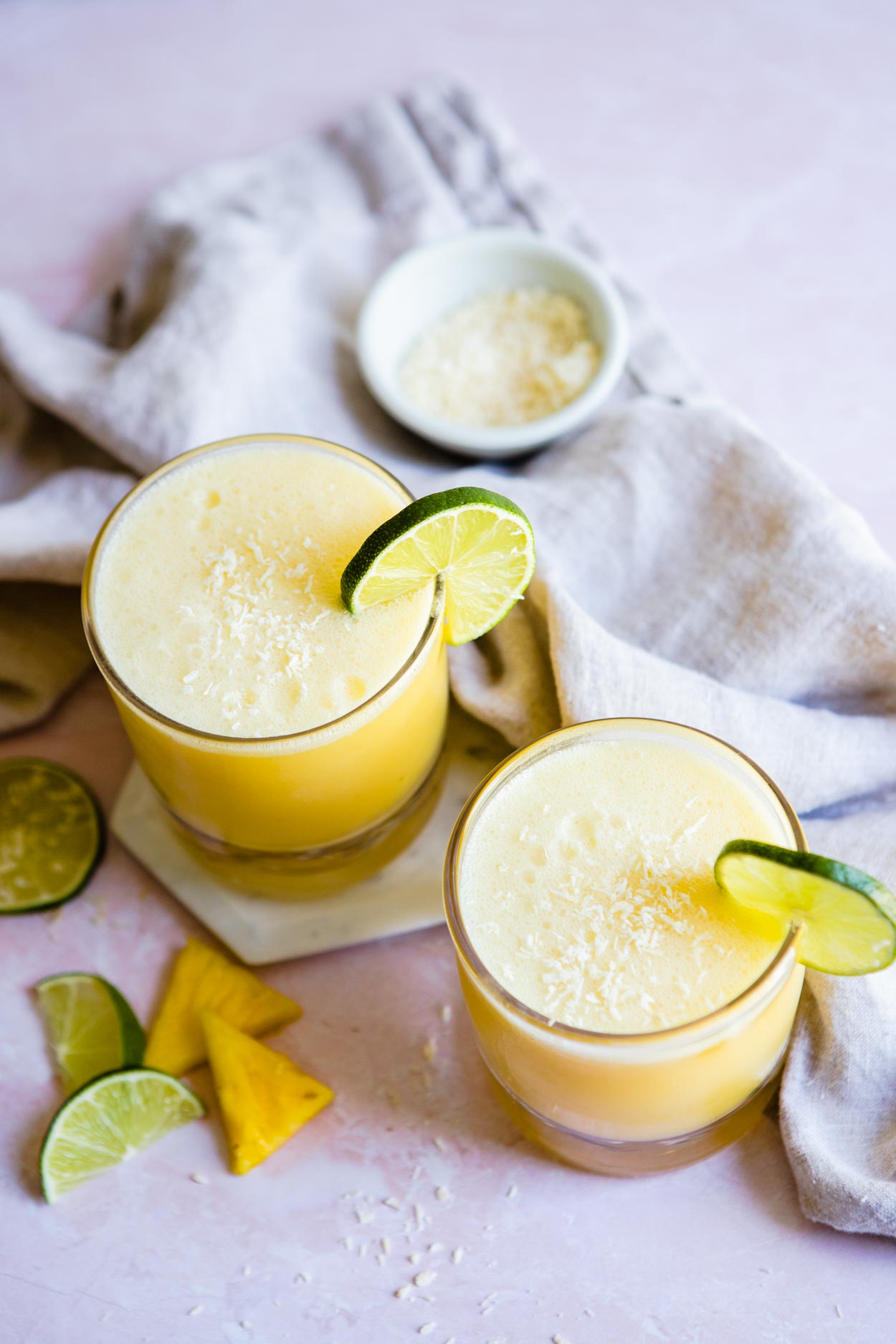 overhead shot of 2 glasses of coconut pineapple margarita with lime wedges and pineapple garnish