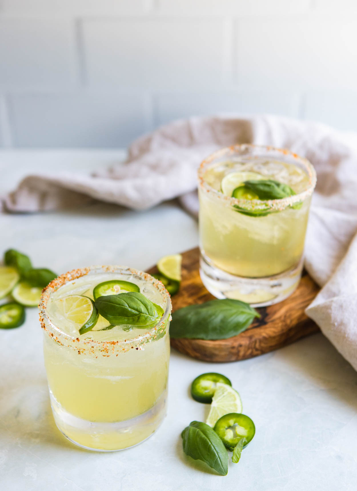 jalapeno margaritas in 2 clear glass tumblers, garnished with jalapeno, cucumber, lime and basil