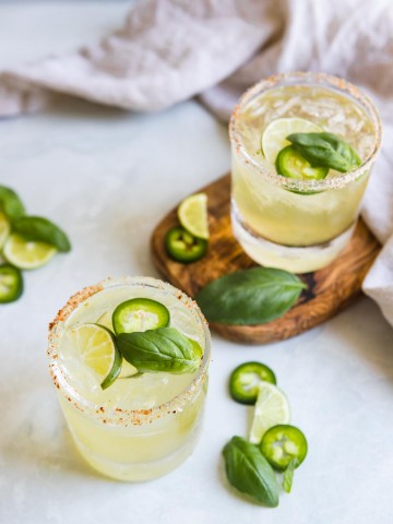 glasses filled with jalapeno margaritas garnished with basil, cucumber and jalapeno