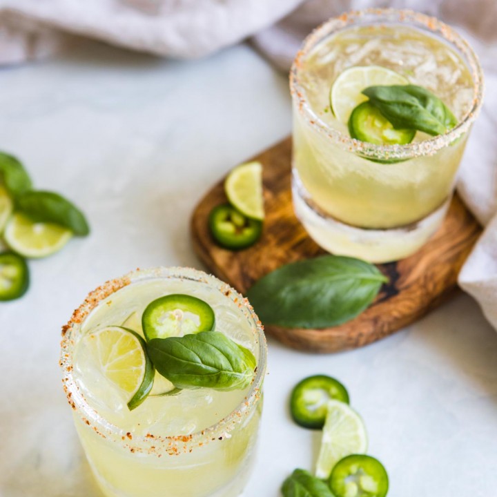 glasses filled with jalapeno margaritas garnished with basil, cucumber and jalapeno
