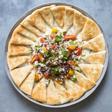 final assembly of layered hummus dip with a full platter of pita bread triangles