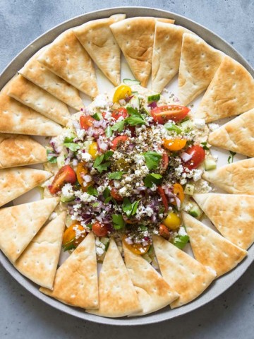 final assembly of layered hummus dip with a full platter of pita bread triangles