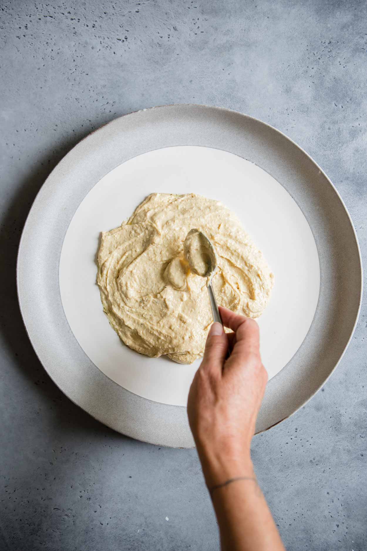 hummus being spread into center of plate with a spoon