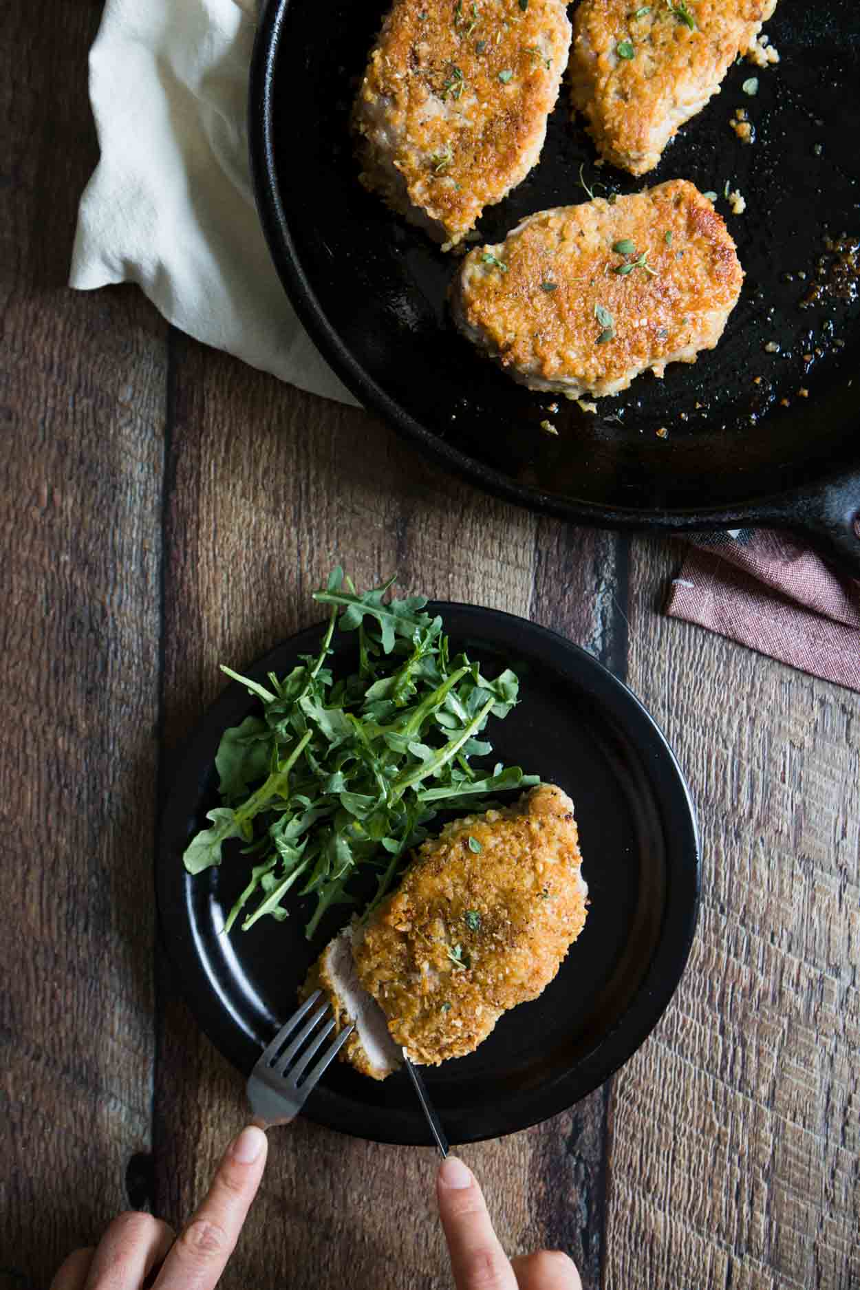 parmesan pork chop on a plate being cut into and a arugula salad