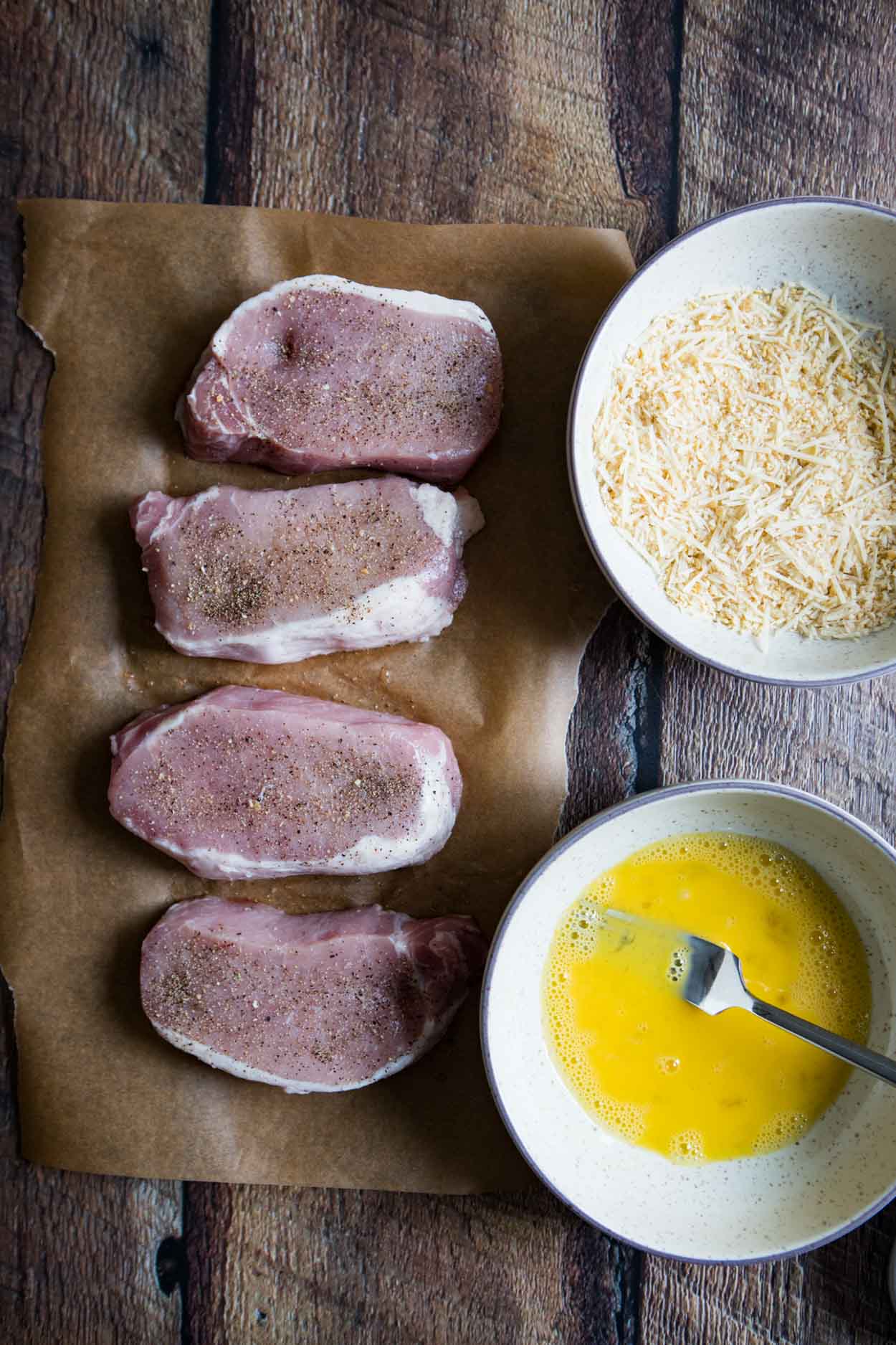 pork chops, bowl of egg, and second bowl of breadcrumbs and parmesan cheese