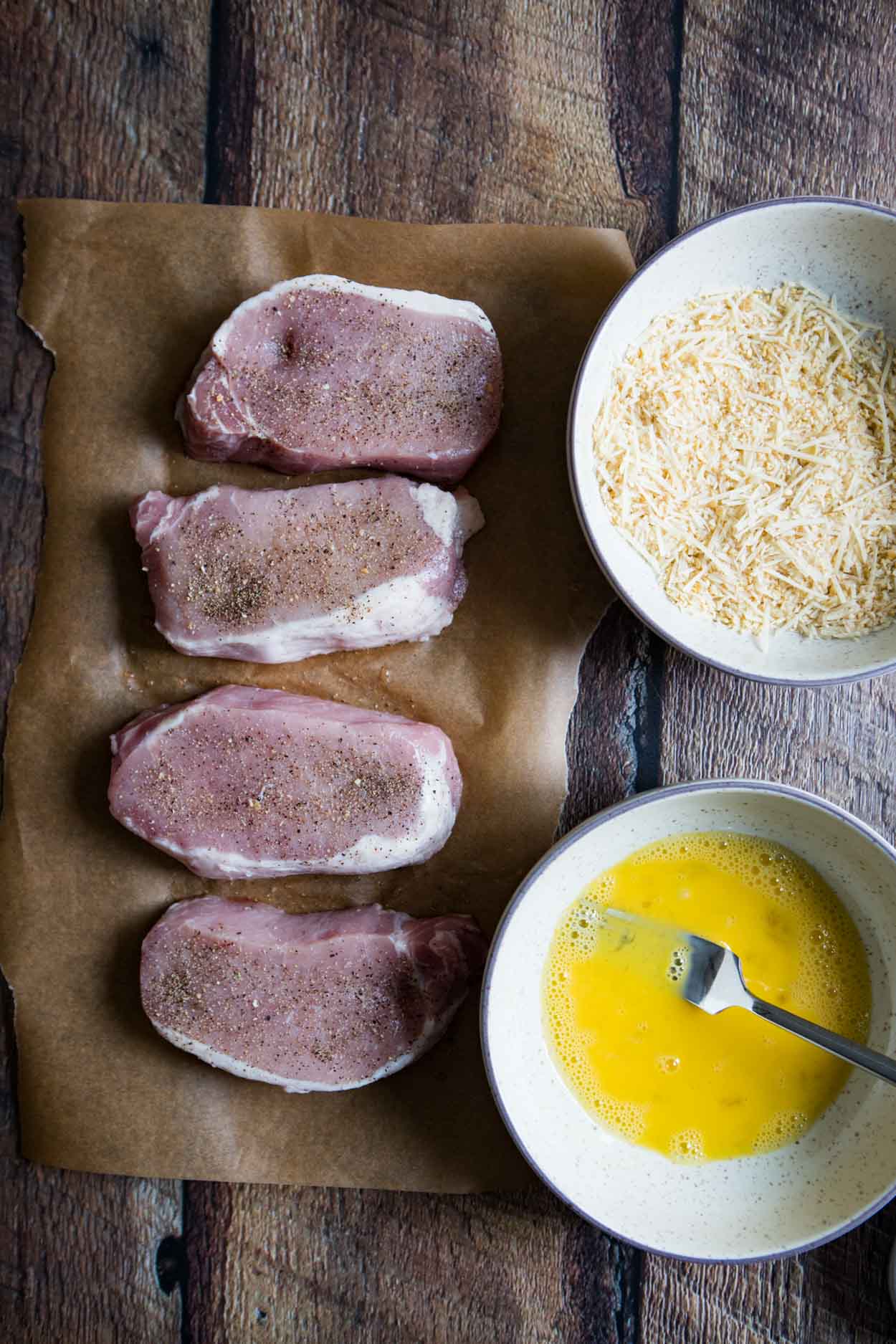 pork chops, bowl of egg, and second bowl of breadcrumbs and parmesan cheese