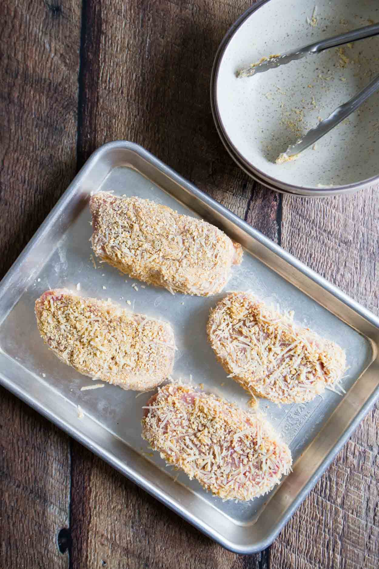 four breaded pork chops on a baking sheet