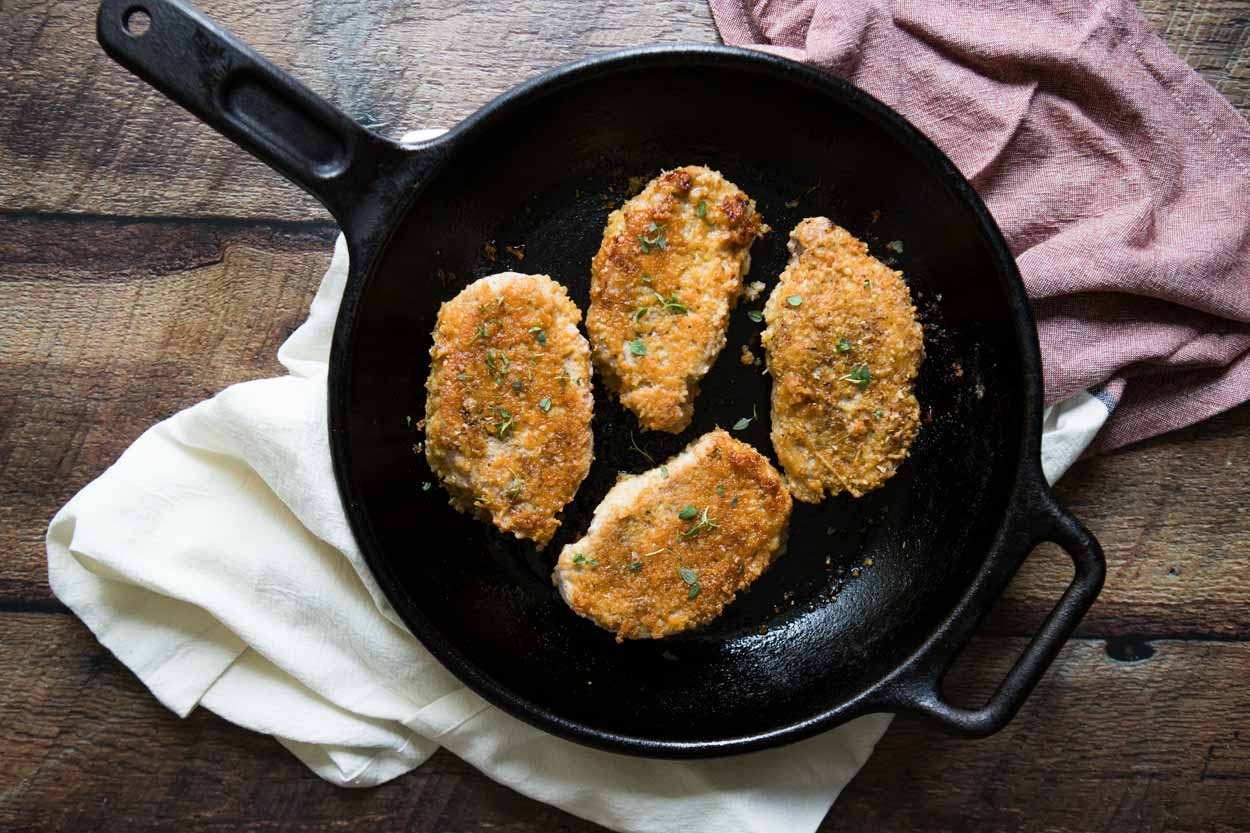 four parmesan pork chops cooked in a cast iron skillet