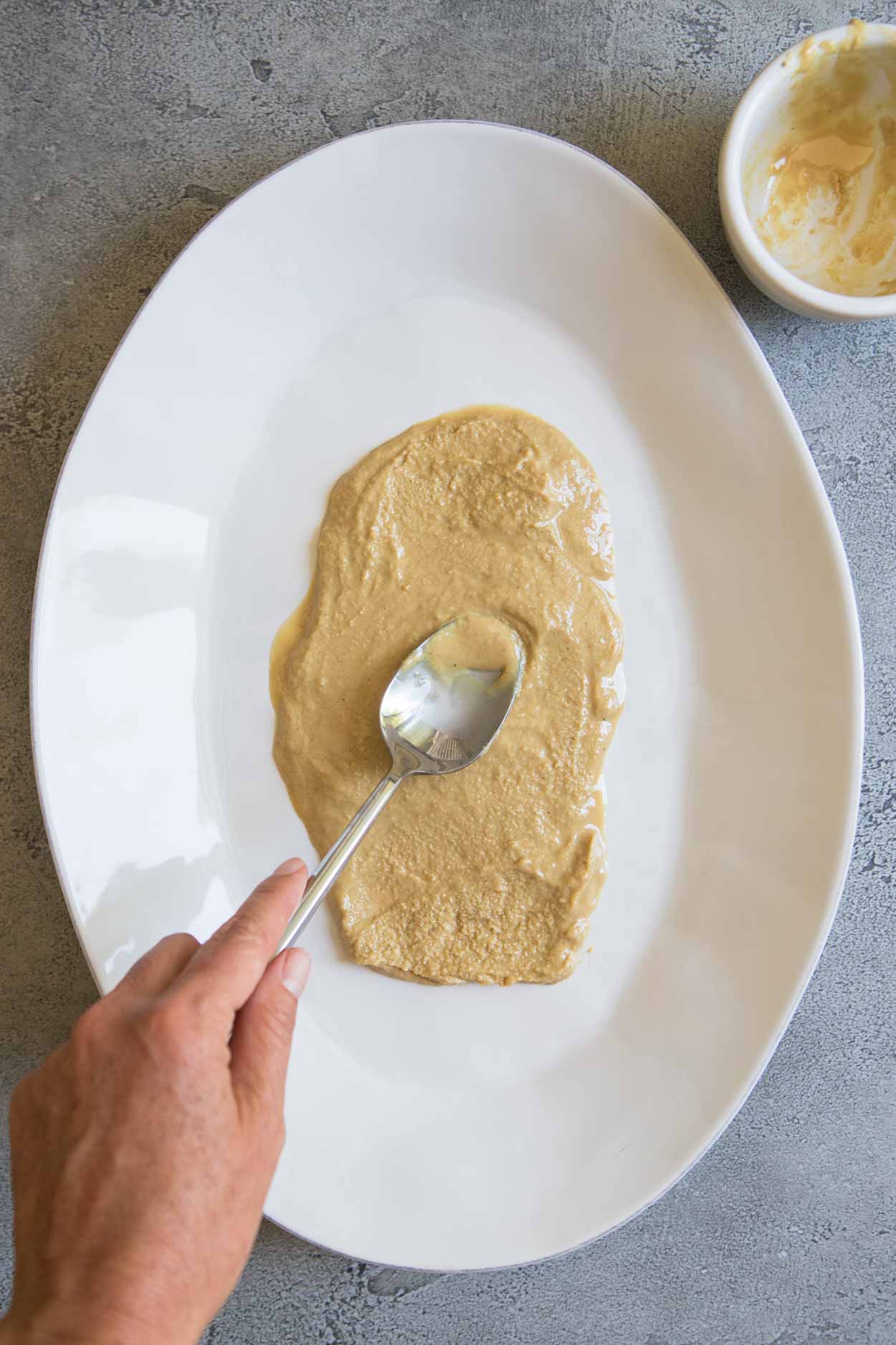hummus being spread on a platter with a spoon
