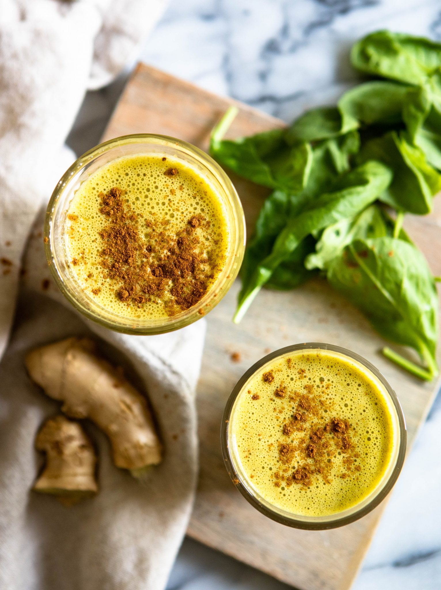 yellow turmeric smoothies in 2 clear glasses with spinach and ginger