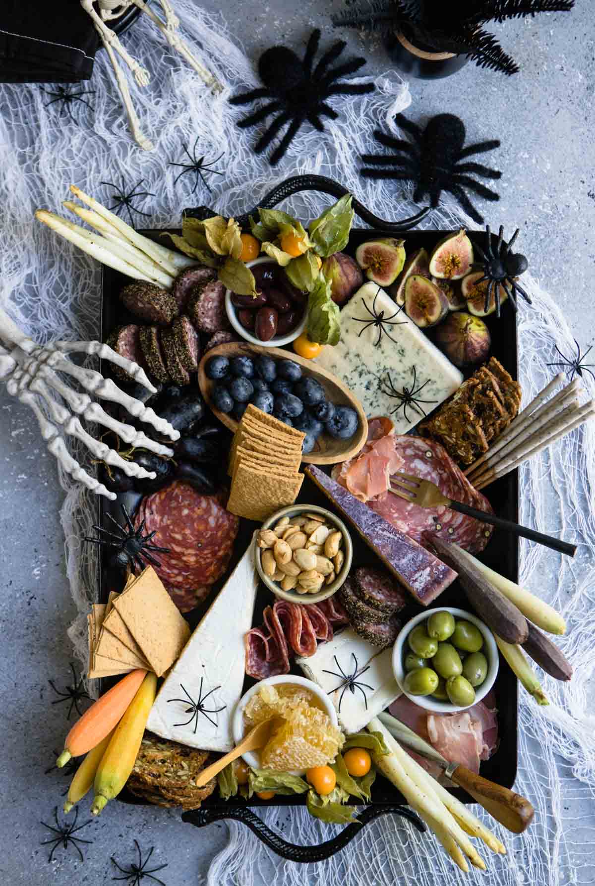 halloween charcuterie board filled with meats, cheeses, crackers and seasonal fruits and decorated with black spiders