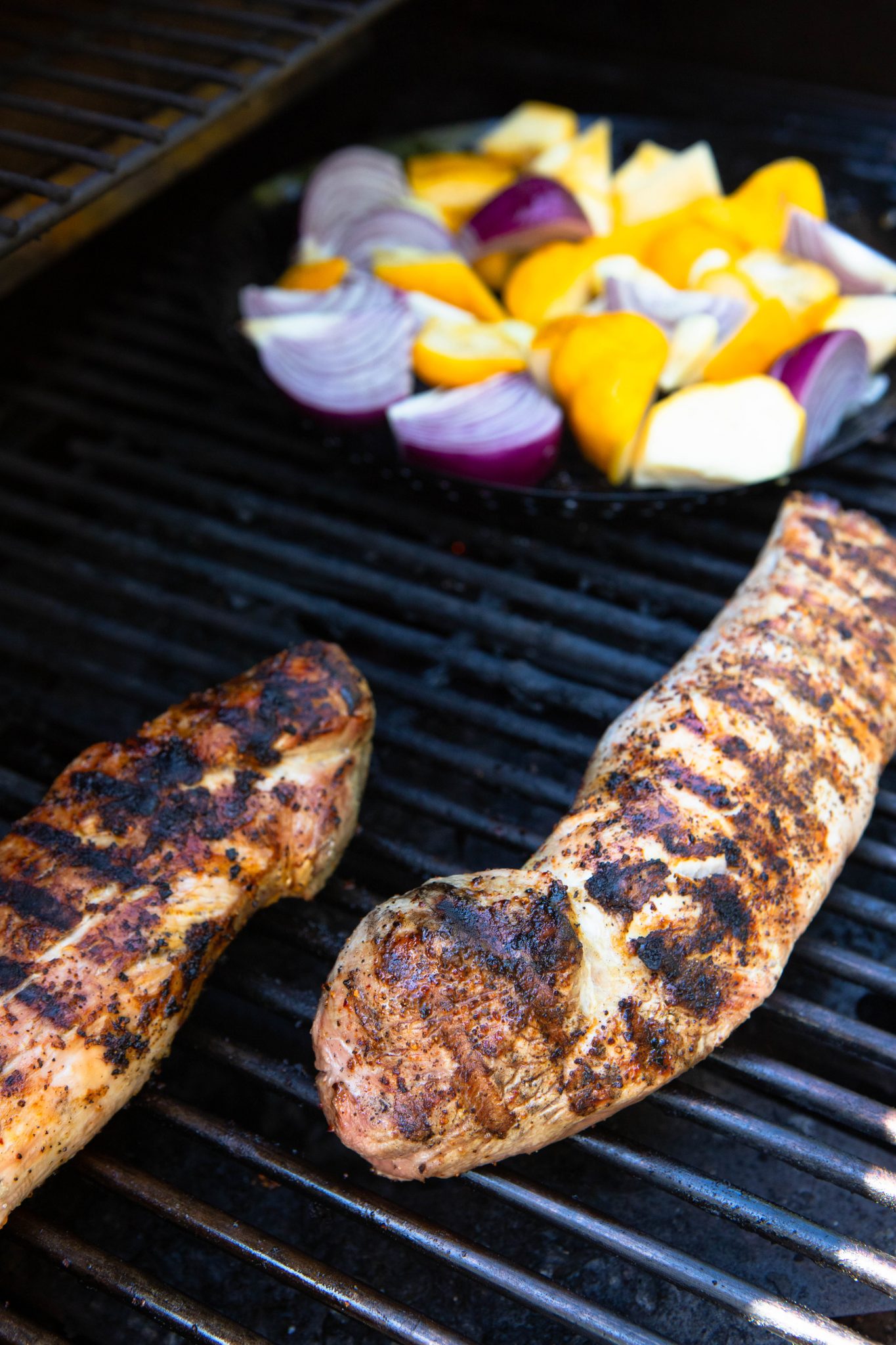 2 pieces of pork tenderloin and summer vegetables on a bbq grill 