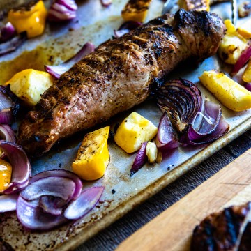 grilled pork tenderloin on a sheet pan with roasted vegetables on a wooden backdrop