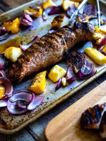 grilled pork tenderloin on a sheet pan with roasted vegetables on a wooden backdrop