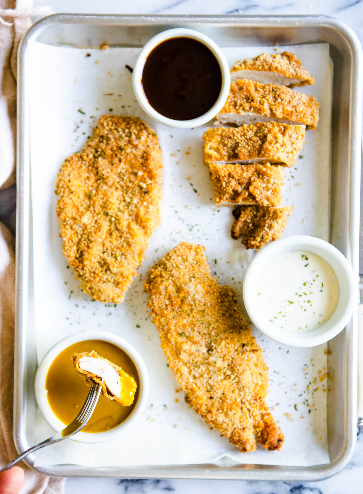 chicken cutlets air fried and resting on a baking tray, with a piece dipped in sauce