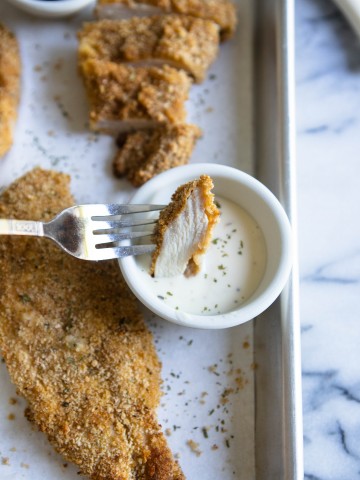 A piece of chicken cutlet cooked in air fryer dipped in ranch dressing