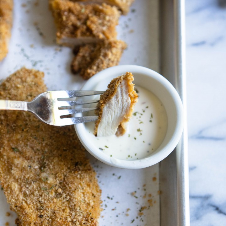 A piece of chicken cutlet cooked in air fryer dipped in ranch dressing