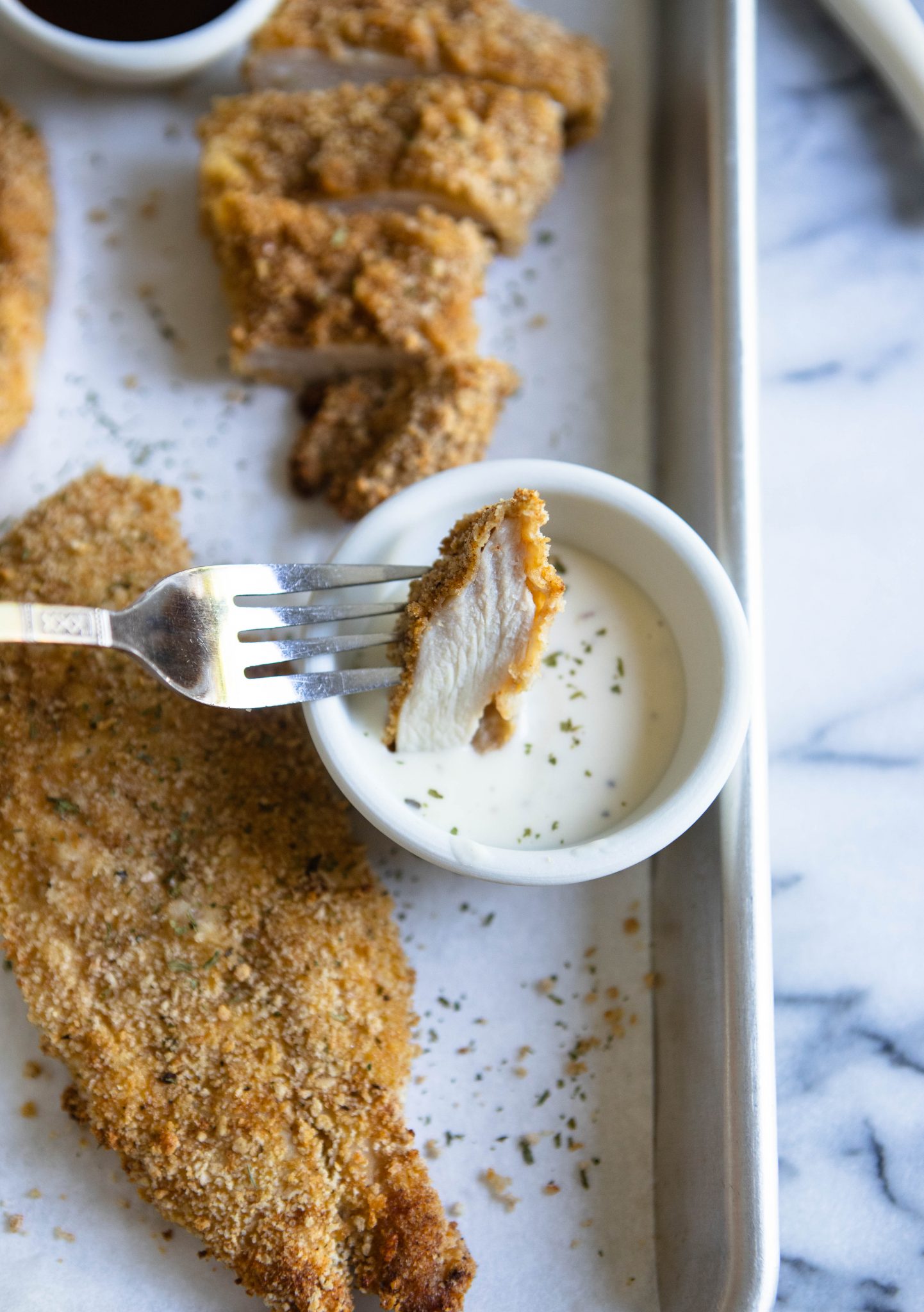 A piece of chicken cutlet cooked in air fryer dipped in ranch dressing