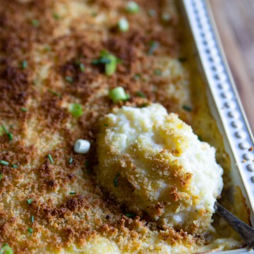 spoon scooping up cheese and potato casserole in a gray dish