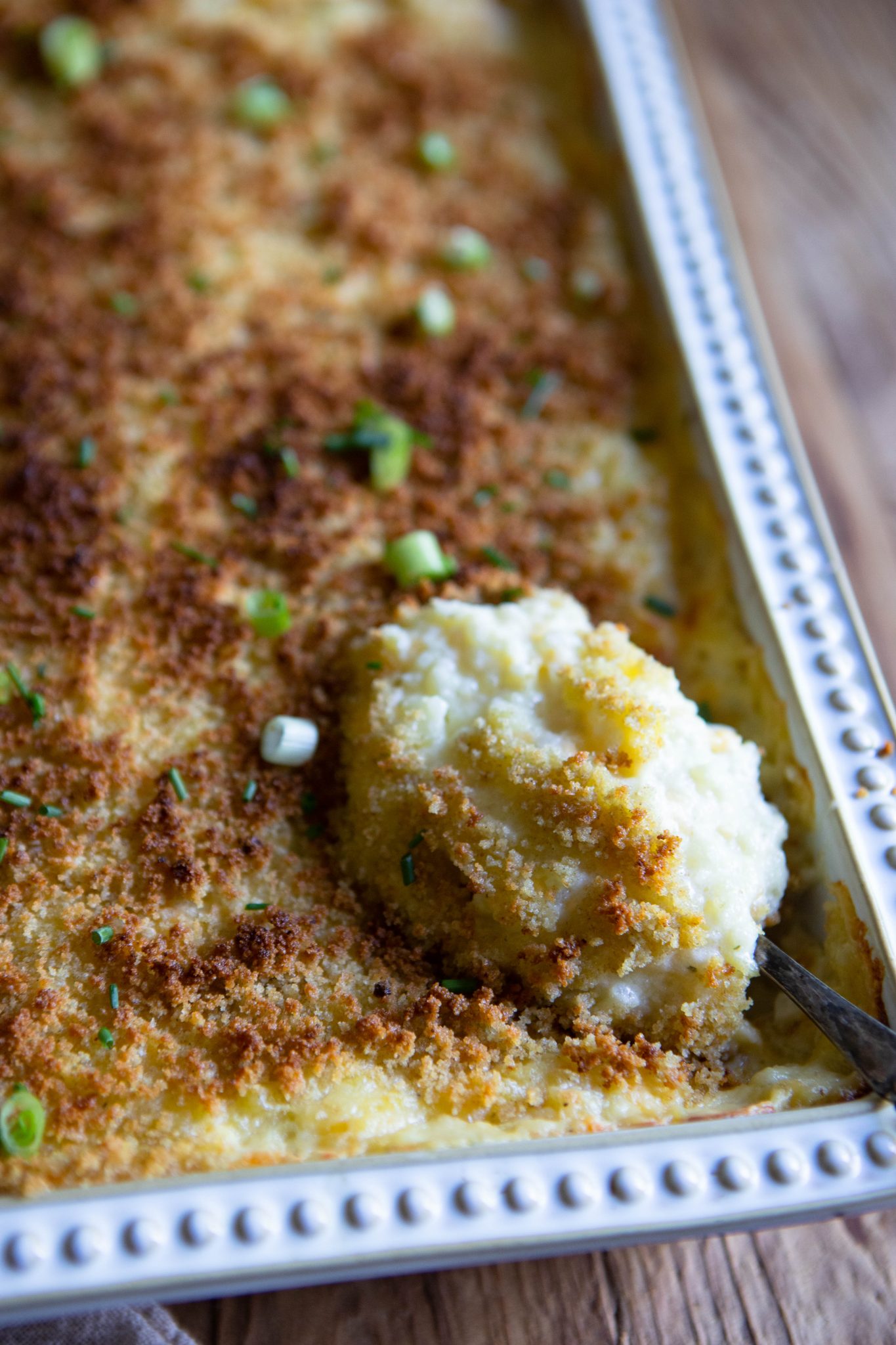 spoon scooping up cheese and potato casserole in a gray dish