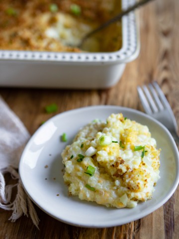 small white plate with cheese and potato casserole served on it, next to a silver fork