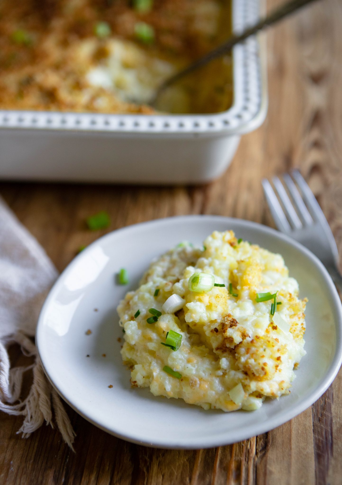 small white plate with cheese and potato casserole served on it, next to a silver fork