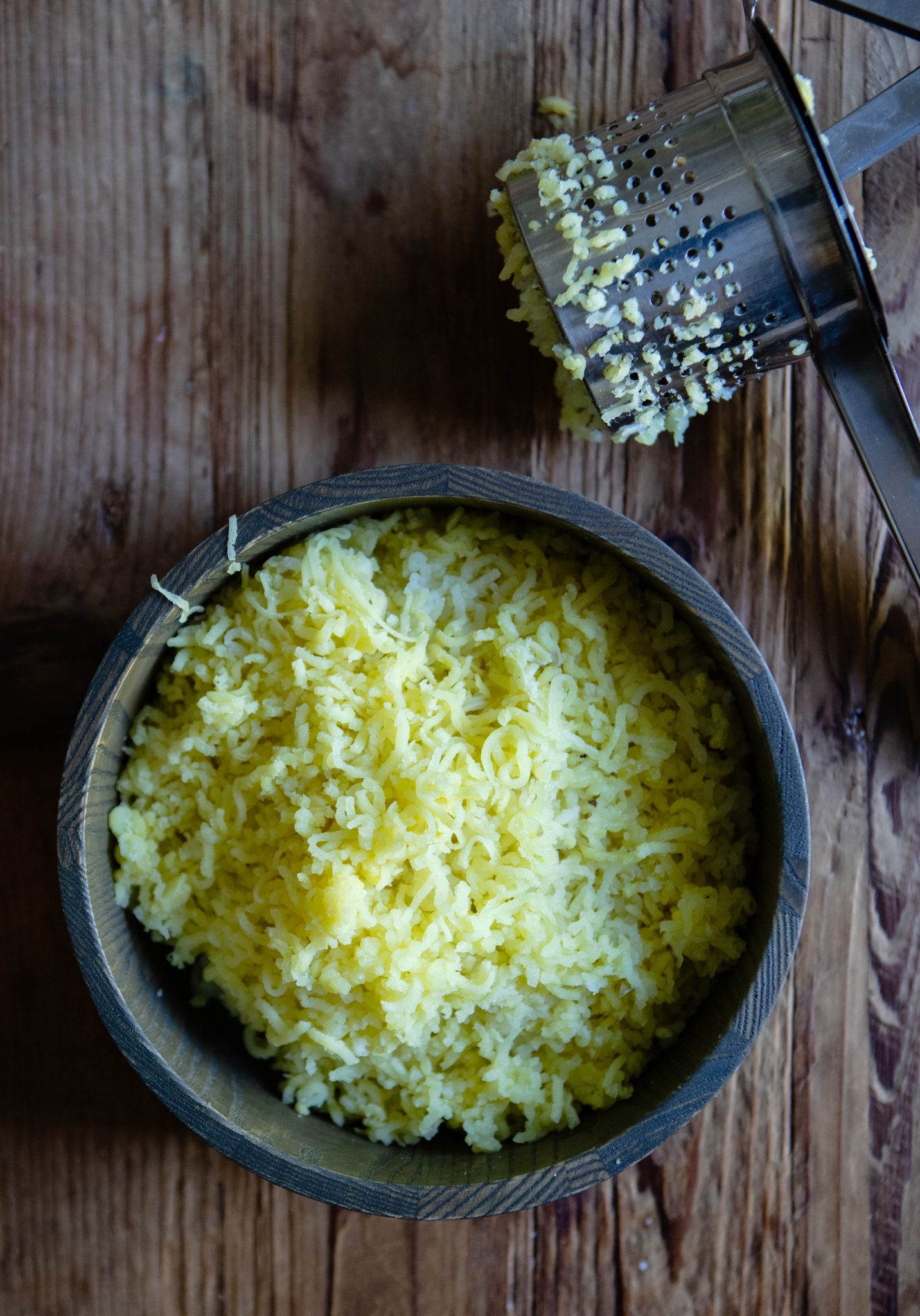 riced potatoes in a wooden bowl, sitting next to a used potato ricer