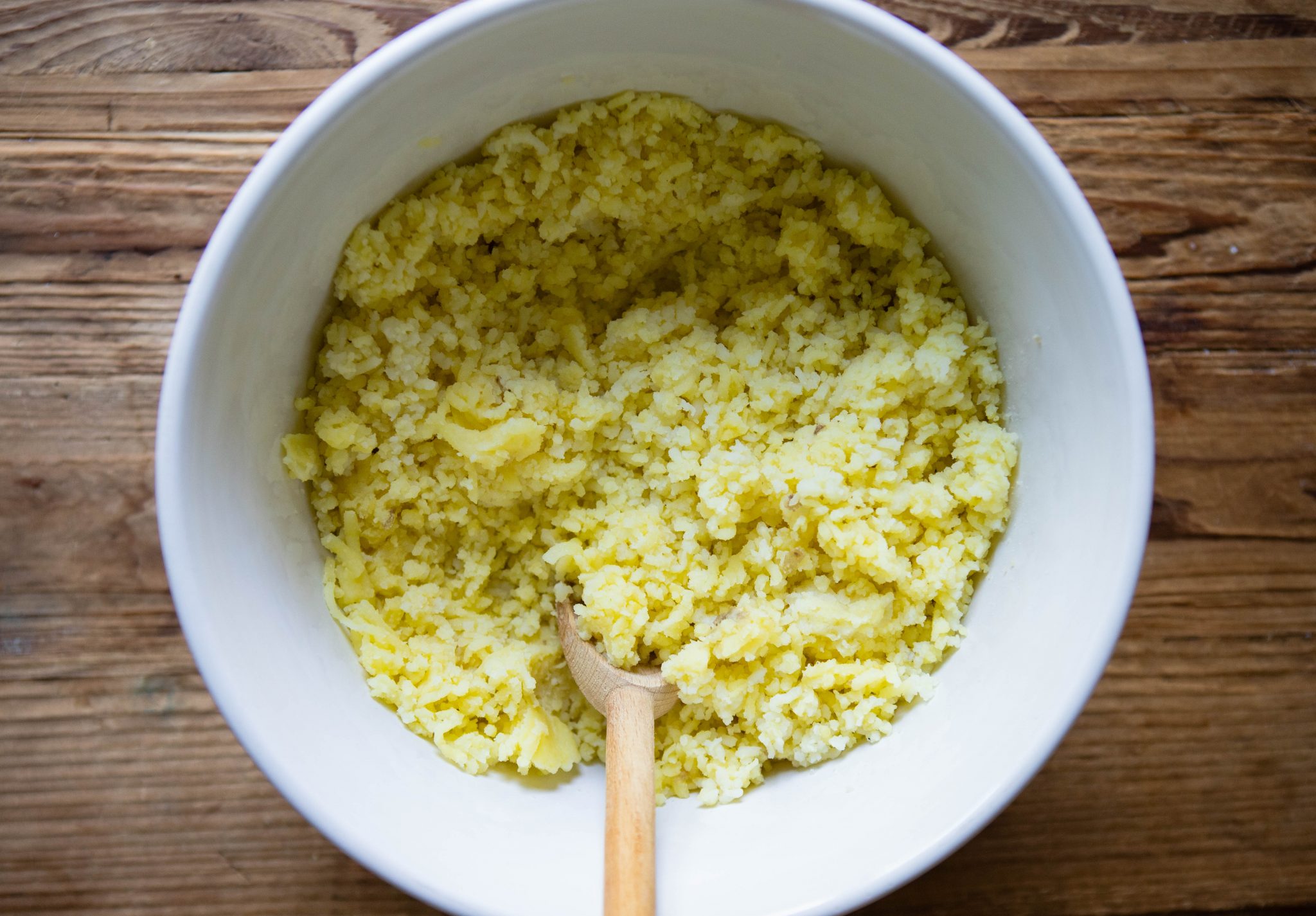 bowl of riced potatoes with a wooden spoon