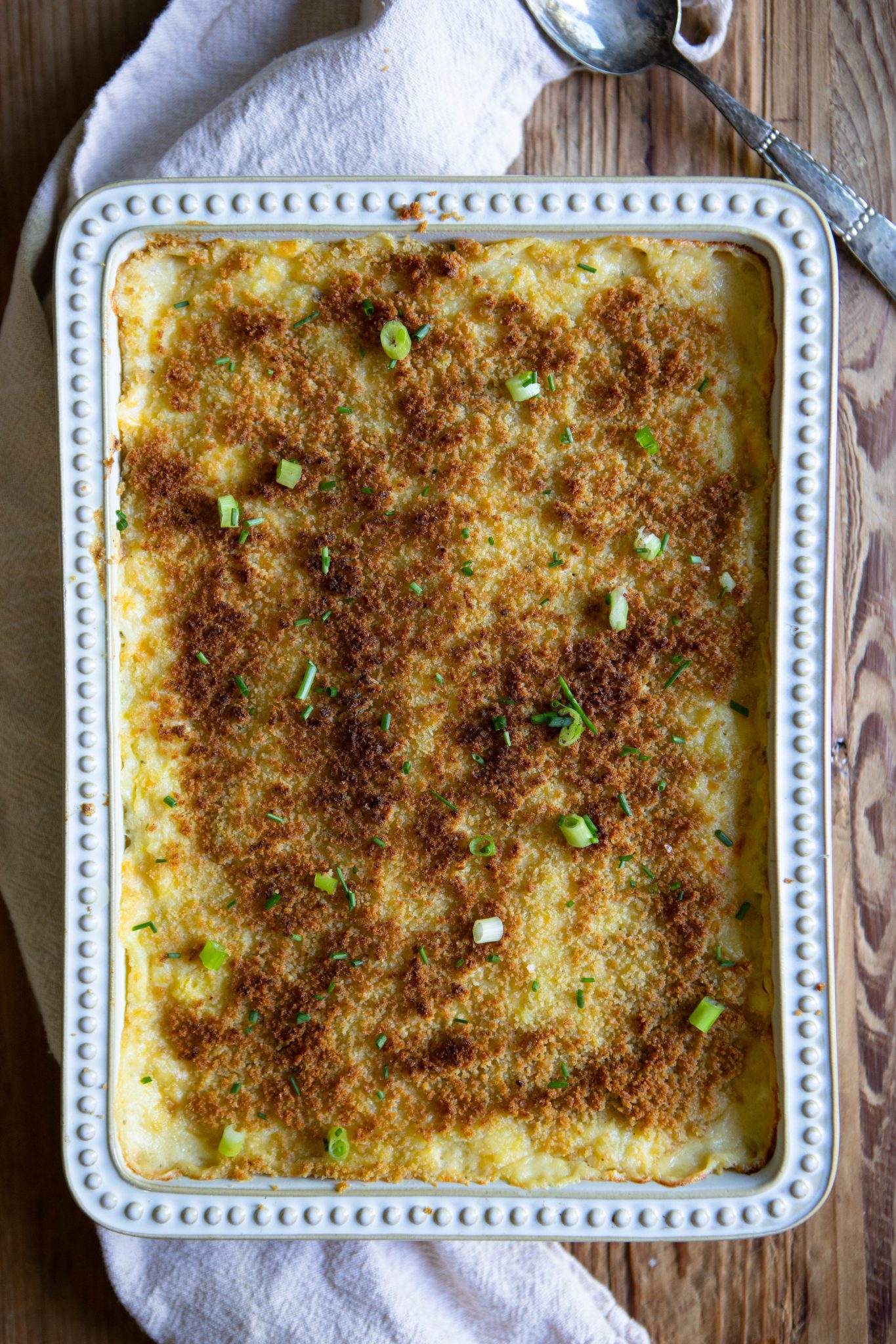 Cheesy potato casserole set on a beige kitchen towel next to a silver serving spoon