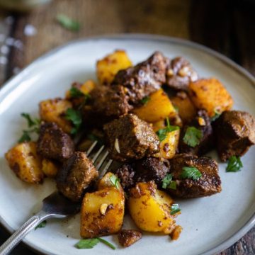 side angle of steak bites with cooked potatoes on a white plate