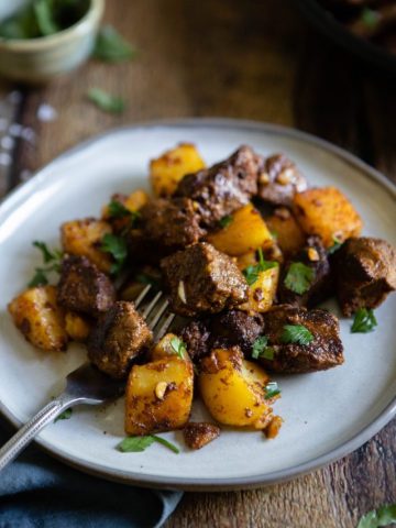 side angle of steak bites with cooked potatoes on a white plate