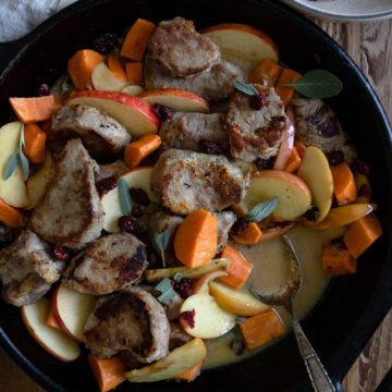 close up of pork, apples and sweet potatoes dinner in a black cast iron skillet