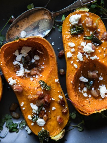 mini butternut squash with pancetta and goat cheese topping on a black platter with an antique spoon