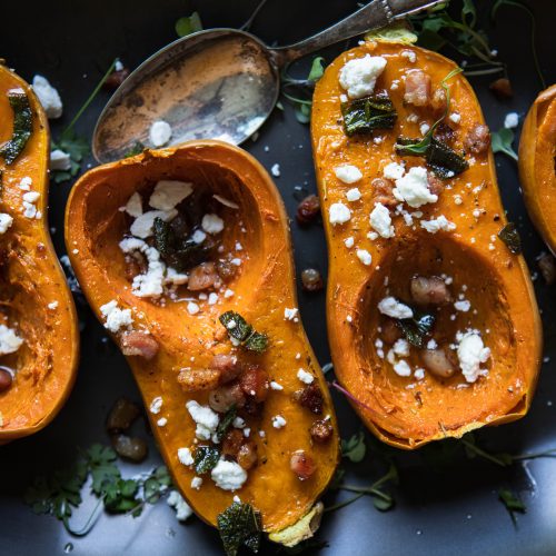 mini butternut squash with pancetta and goat cheese topping on a black platter with an antique spoon