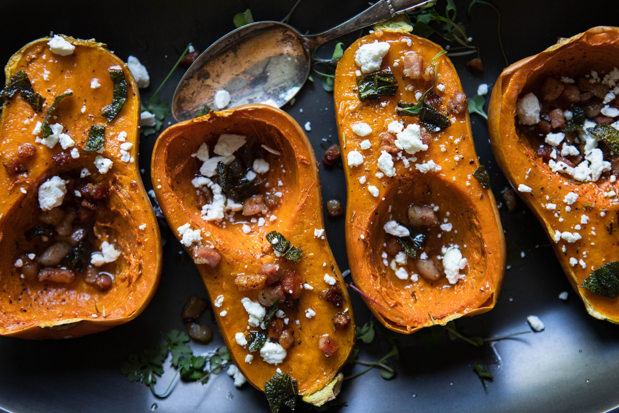 mini butternut squash with pancetta and goat cheese topping on a black platter with an antique spoon